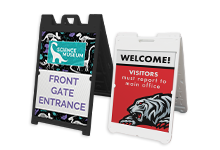 Two freestanding A‑frame sidewalk signs displaying full‑color printed graphics, commonly used for event directions, promotions, and business signage.